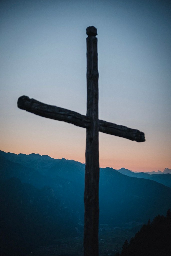 A cross with mountains in the background and a colorful sky.